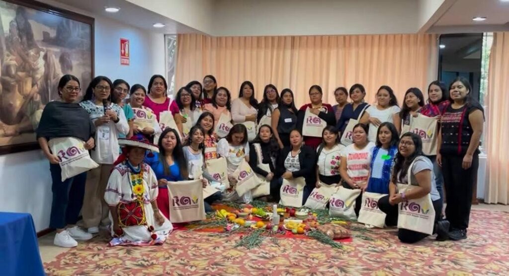 Foto con varias mujeres, incluidas integrantes de la Red de Abogadas Indígenas, en un espacio cerrado. Ellas están acomodadadas en 2 filas en forma de semicírculo, unas paradas y otras hincadas. En medio parec haber una ofrenda con fruta, velas y algunas hierbas.